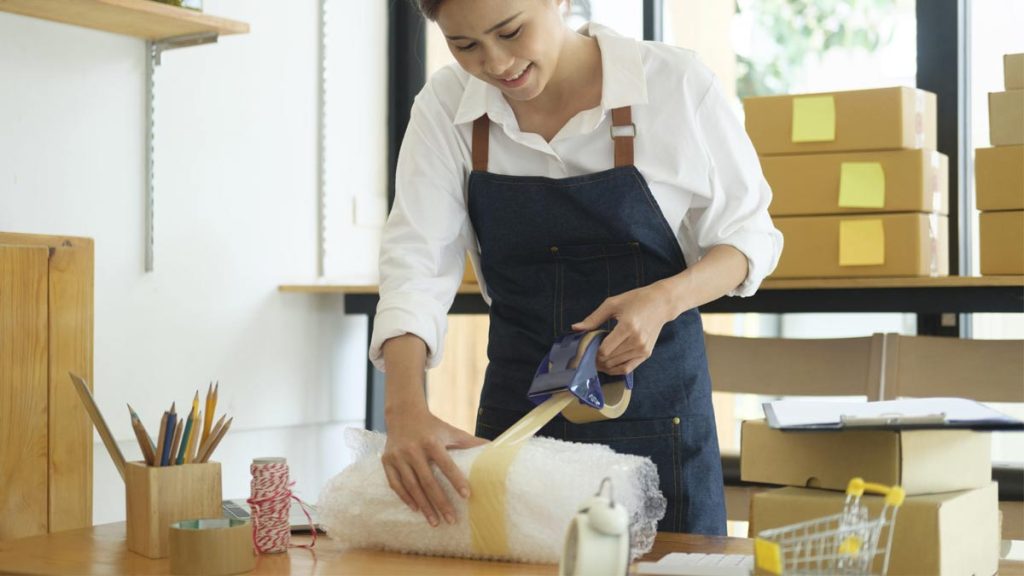 شماره تلفن کار در منزل بسته بندی - زن در حال بسته بندی کالا و چسب کردن آن می باشد